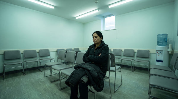 A woman waiting alone in a row of chairs in a clinic waiting area under fluorescent light