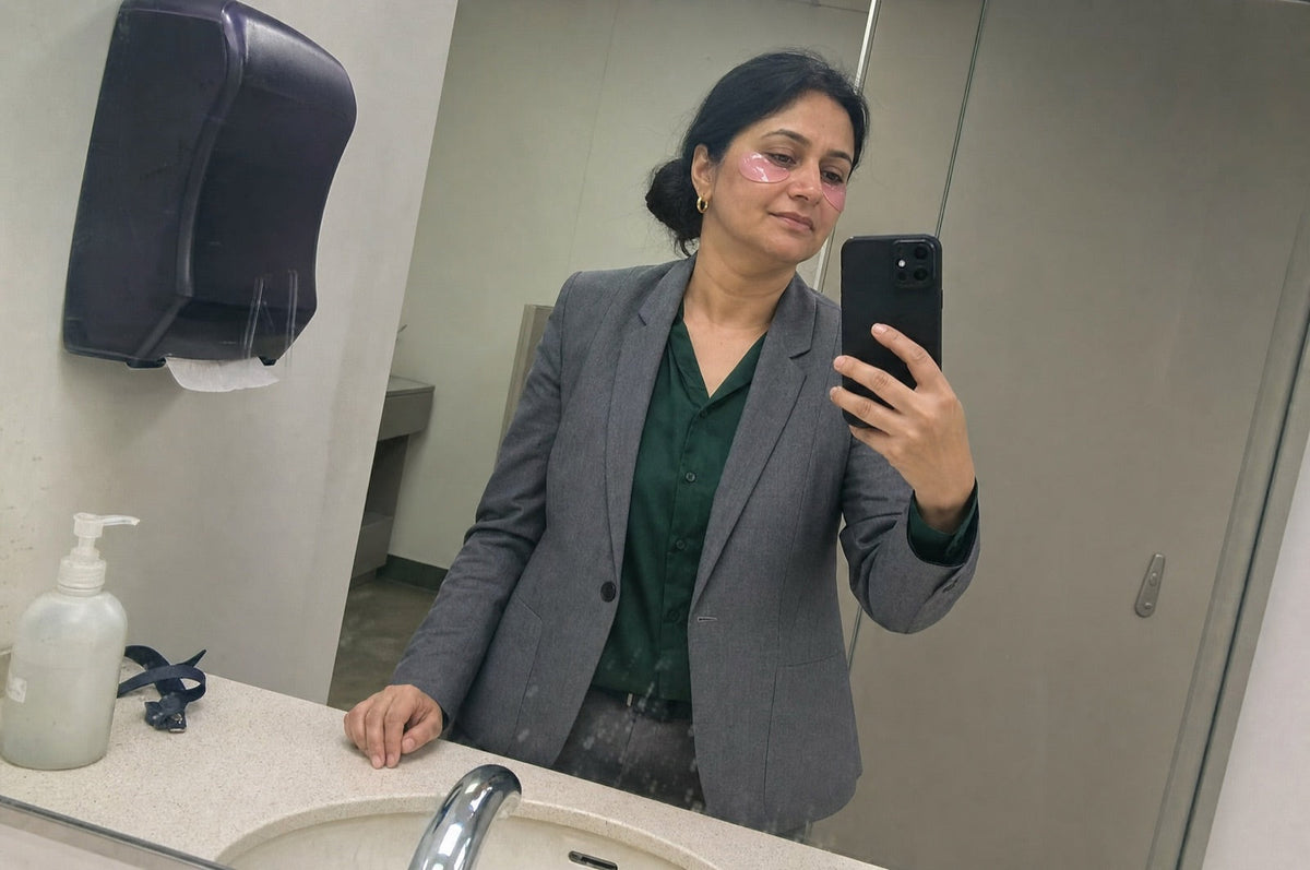 Woman in her forties taking a mirror selfie in an office washroom with pink hydrogel patches under her eyes