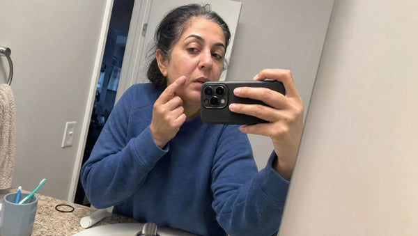 Woman in her early fifties taking a bathroom mirror selfie while touching a dry patch on her cheek