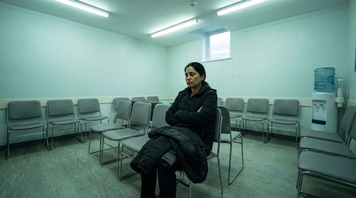 A woman waiting alone in a row of chairs in a clinic waiting area under fluorescent light