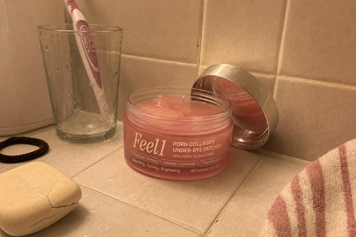 Open jar of Feel1 PDRN Collagen Under-Eye Patches on a tiled bathroom shelf, chrome lid leaning behind it